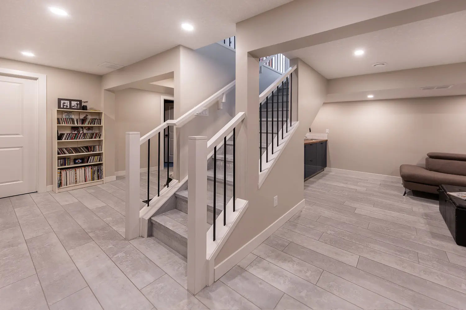 Modern basement interior with staircase, bookshelf, and sofa.