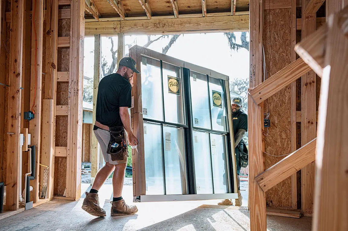 Person walking through a home construction site with large windows and wooden framing.